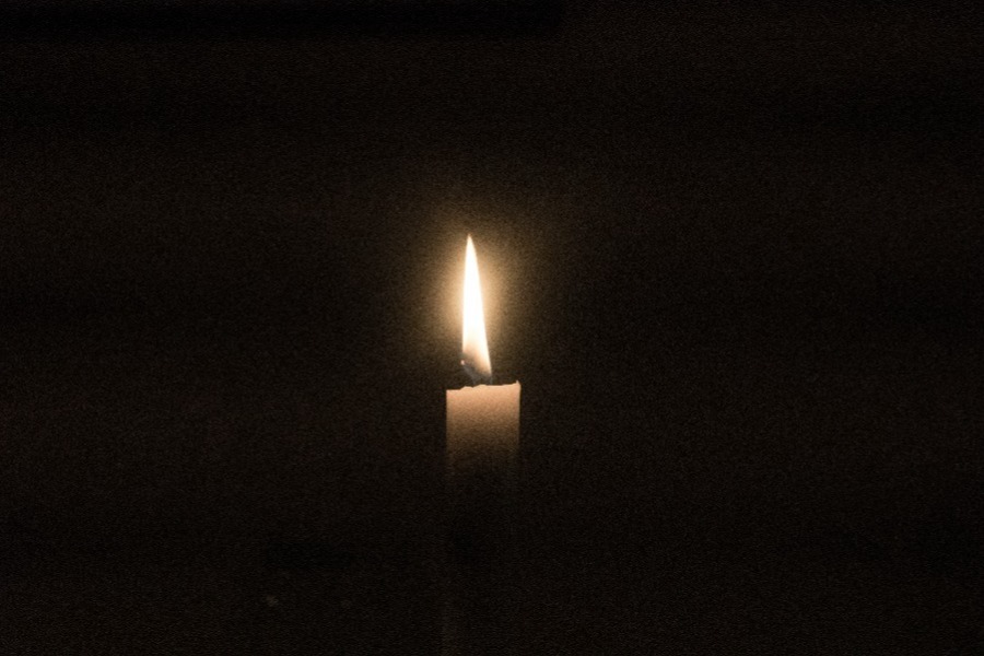 Eine brennende Kerze im Dunkeln, Sinnbild für die Hoffnung, die weiterbrennt, auch wenn wir sie nicht sehen.