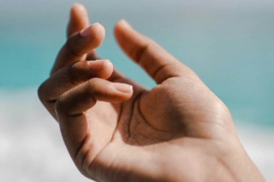 Eine geöffnete Hand vor Himmel und Meer, Sinnbild für das Loslassen, das zugleich ein Empfangen ist.