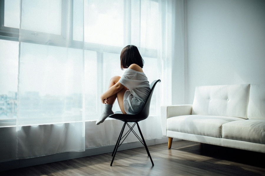 Frau sitzt allein auf einem Stuhl in einem Zimmer, Sinnbild für die Schwere einer depressiven Verstimmung
